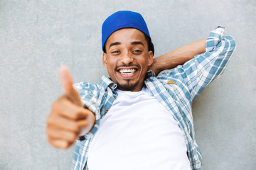 Naklejka premium Smiling young african guy laying on a concrete outdoors