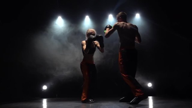 Guy with a girl boxing gloves beating in the ring . Light from behind. Smoke background. Slow motion