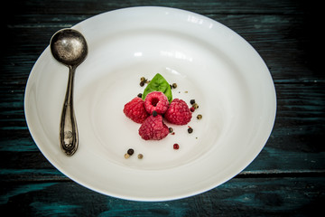 Red raspberry dessert / Fresh ripe fruit served on a white plate with cutlery on dark background. Minimalistic concept with copy space
