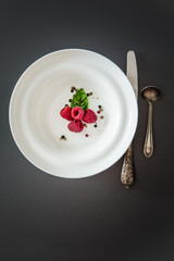 Red raspberry dessert / Fresh ripe fruit served on a white plate with cutlery on dark background. Flat lay minimalistic concept with copy space