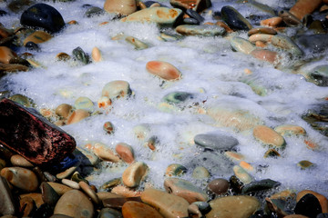 Sea foam covers the colorful sea pebbles that Shine in the sun.