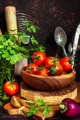 Fresh tomatoes and parsley, dill, garlic on a dark background in a rustic kitchen and wooden utensils still life with copy space