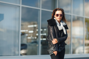 Fototapeta premium woman in sun glasses a black leather jacket, black jeans posing in front of mirrored windows. Female fashion concept. Outdoor