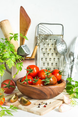 Fresh tomatoes and parsley, dill, garlic on a light background in a rustic kitchen and wooden utensils still life with a copy space