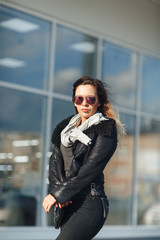 woman in sun glasses a black leather jacket, black jeans posing in front of mirrored windows. Female fashion concept. Outdoor