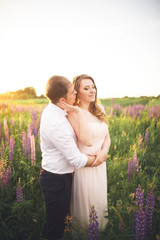 Emotional beautiful bride hugging newlywed groom from behind sunset at a field closeup