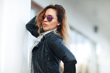 woman in sun glasses a black leather jacket, black jeans posing in front of mirrored windows. Female fashion concept. Outdoor