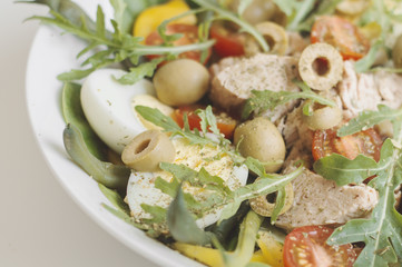 Bowl with fresh salad: olives, tuna fish, eggs, arugula leaves, spinach, cherry tomato, cucumber, green beans and yellow peper. Nicoise salad