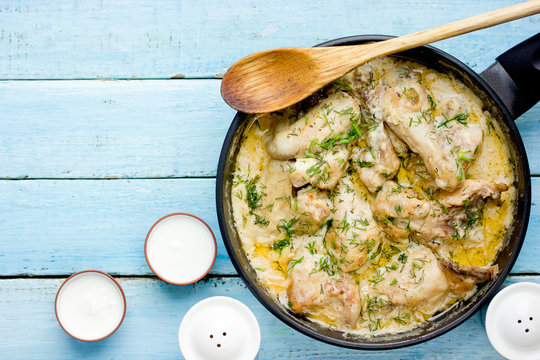 Gedlibzhe &mdash; kabardian chicken in sour cream sauce with onion served in black frying pan on a blue wooden background with ingredients top view