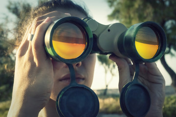 A girl looking at the horizon through a pair of military binoculars. Big mojo front shot.
