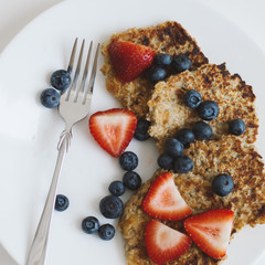 Whole grain pancakes with blueberry and strawberry served on white plate with silver fork, square photo