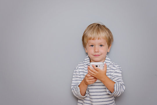 Cute three years old boy holding smartphone on grey background with copy space