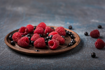 Blueberries and raspberries in an old-fashioned container on a gray concrete background