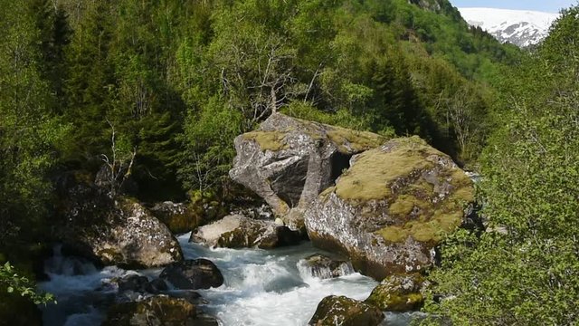 The river Jordalselvi with the glacier Buerbreen in the background. The river runs in a mountain valley with steep slopes.