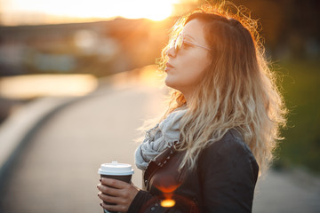 Attractive woman in mirrored sunglasses, a black leather jacket, drinking coffee on the waterfront...