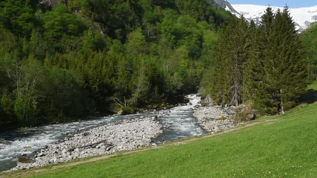 The river Jordalselvi with the glacier Buerbreen in the background. The river runs in a mountain valley with steep slopes.