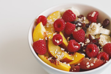Breakfast meal: quick cook oats, plum, nectarine slices, banana, dried cranberry and fresh raspberry in a big bowl on white table