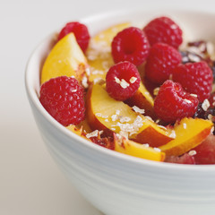 Square photo of healthy vitamin breakfast. Raspberry, nectarine, plum, dried cranberry, banana and oats in a blue bowl. Fruit salad
