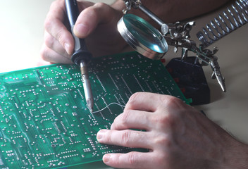 Repair circuit board with soldering iron and magnifying glass