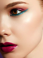 Cosmetics products. Close up of cheerful young woman with colorful makeup. Beauty portrait of female model with vivid makeup on violet background