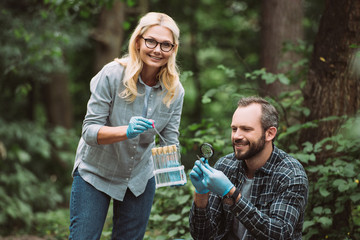 selective focus of male and female scientists examining and taking sample of dry leaf in forest