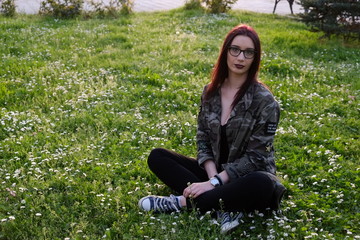 Military style girl sitting in a park on a grass full with flowers