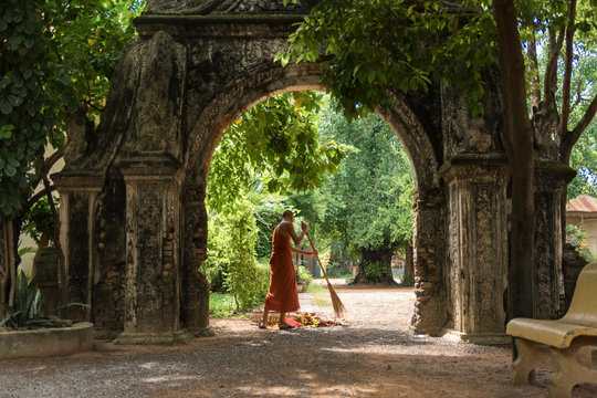 Buddhist monks sweeping under a stone arch in Buddhist temple in cambodia