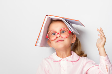 ittle girl preschooler wearing glasses keeps an open book on her head