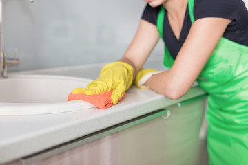 Closeup of female hands in rubber yellow gloves cleaning the cooker panel at home kitchen. Home,...