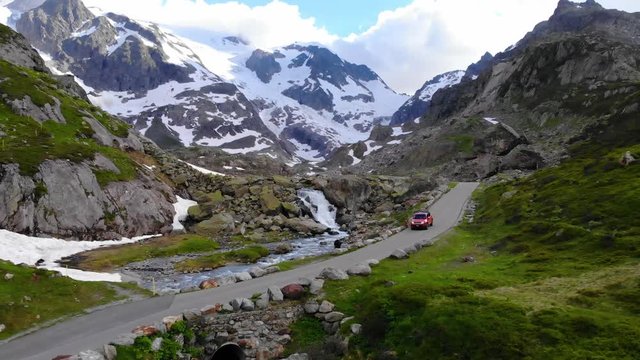 Aerial shot over a waterfall to reveal the Steingletscher in Switzerland with a Jeep driving past a man flying a drone