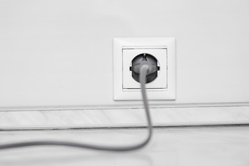 Electric white socket and one plugged in power cord on white wall background