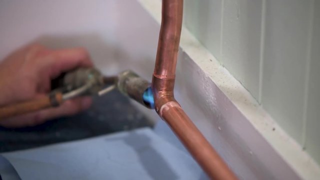 Plumber soldering copper pipes with blow torch burner. Close up.
