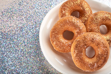 Top view of plate with baked bagels covered with golden glitters and arranged on silver glowing surface 
