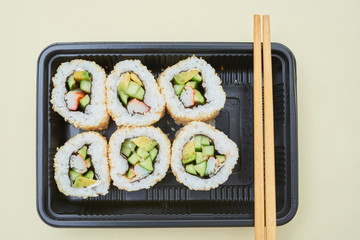 Top view of small black container filled with freshly made sushi and served with chopsticks on white surface