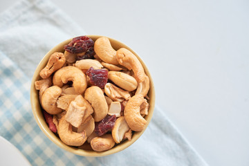 Top view of small bowl filled with healthy snack of cashew nuts and sweet dried fruits on table