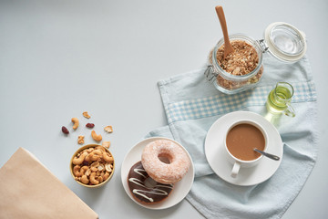 From above shot of coffee cup served with doughnuts and granola in jar on table with nuts