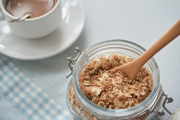 Close-up shot of glass jar filled with flake of granola and served with wood spoon on table