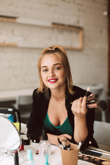 Pretty smiling beauty blogger dreamily looking in camera holding make up brushes in hand while recording new video for vlog