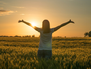 A sillhouette of a happy woman standing in a wheat field in summer.