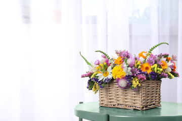 Wicker basket with beautiful wild flowers on table against light background