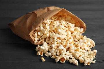 Paper bag with tasty popcorn on wooden background