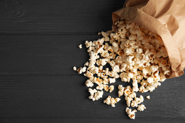 Paper bag with tasty popcorn on wooden background