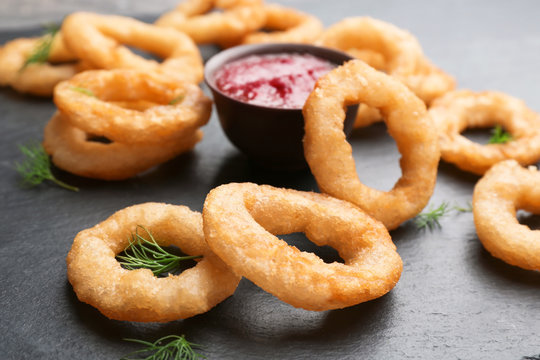 Fried onion rings and bowl of sauce on table, closeup