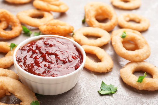 Fried onion rings and bowl of sauce on grey background, closeup