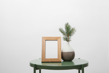Blank frame and vase with fir branch on table against white background. Mock up for design