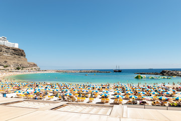 Las Americas, Canarias islands/ Spain-July 22, 2018: View of beach fool of tourists and umbrellas for sun on Canarias, view of bay with mountains. Blue Atlantic ocean and beach on Gran Canaria.