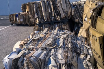 Bales of compressed corrugated kraft cardboard in outdoor storage showing layers of material