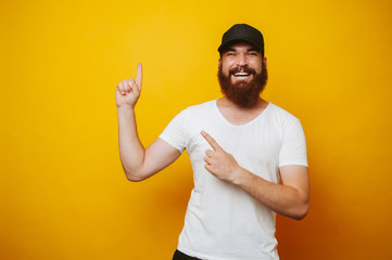 Happy bearded man in white t-shirt pointing up at copyspace