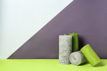 Different decorative wax candles on table against color background