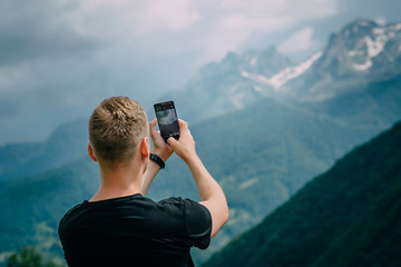 man photographs mountains smartphone camera